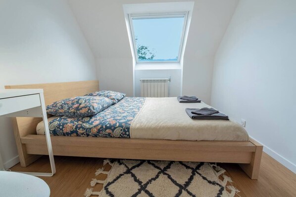 A bedroom with a wooden bed, a skylight, a radiator, and a patterned rug.