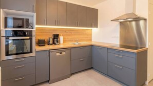 Une cuisine moderne avec des meubles gris, une hotte en acier inoxydable, un four encastré et un lave-vaisselle.