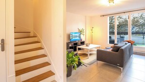 Un salon moderne avec un escalier, un téléviseur à écran plat, un canapé et une grande fenêtre offrant une belle vue.