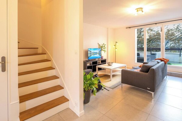 Ein modernes Wohnzimmer mit Treppe, Flachbildfernseher, Sofa und großem Fenster mit Aussicht.