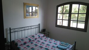 A bedroom with a bed, a bedside table, a window, and a framed picture on the wall. - Villa Bellavista (Quartu Sant'Elena)