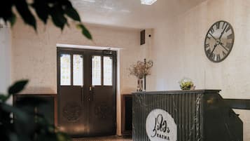 Zona de recepción con un reloj grande, mostrador de recepción y puerta con paneles de vidrio decorativos.