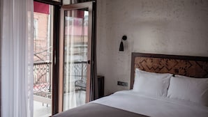 Ein Hotelzimmer mit Bett, einem Fenster mit Vorhängen, Blick auf den Außenbalkon und einer Wandleuchte.