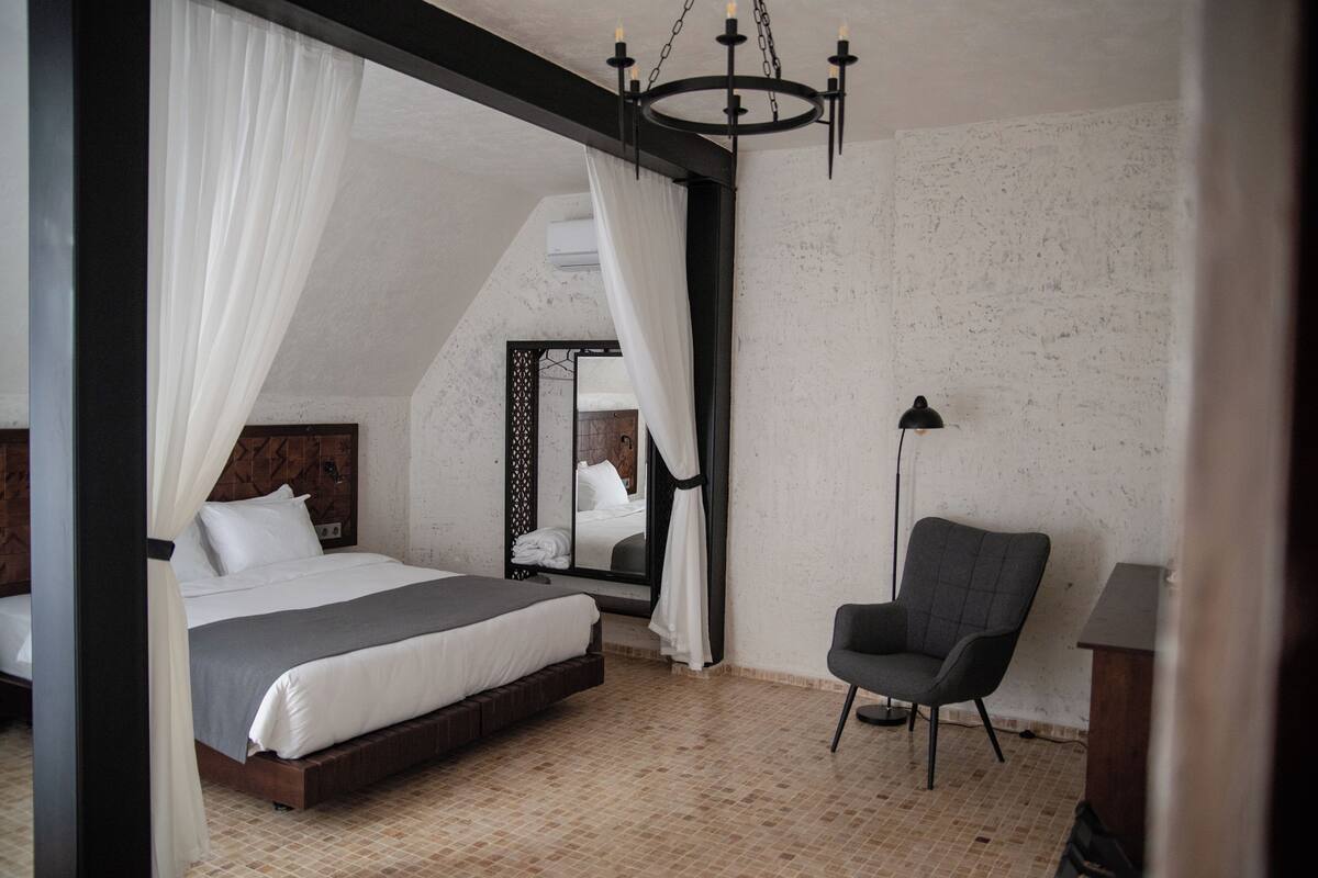 Ein Schlafzimmer mit Bett, Stuhl, Spiegel und einer Chandeliebre.