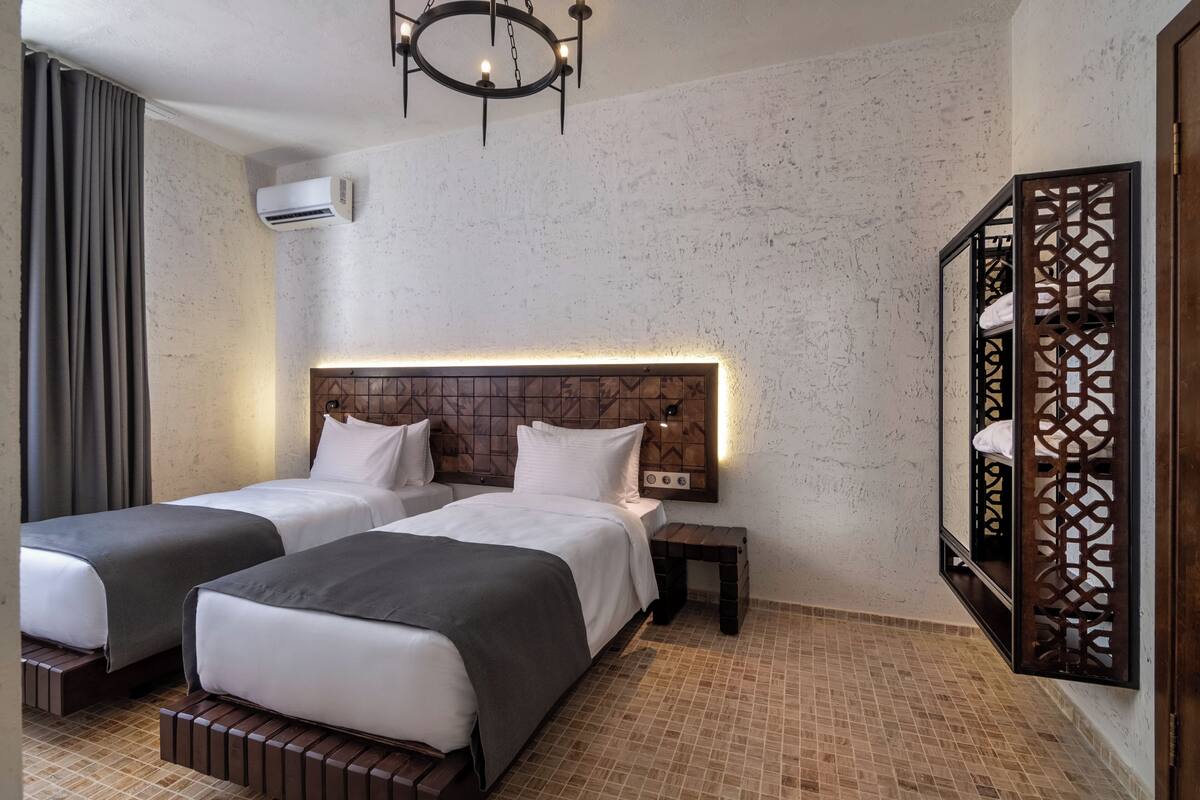 Ein Hotelzimmer mit zwei Betten, einem Holzkopfstück, einem Nachttisch, einem Spiegel und einem Fliesenboden.