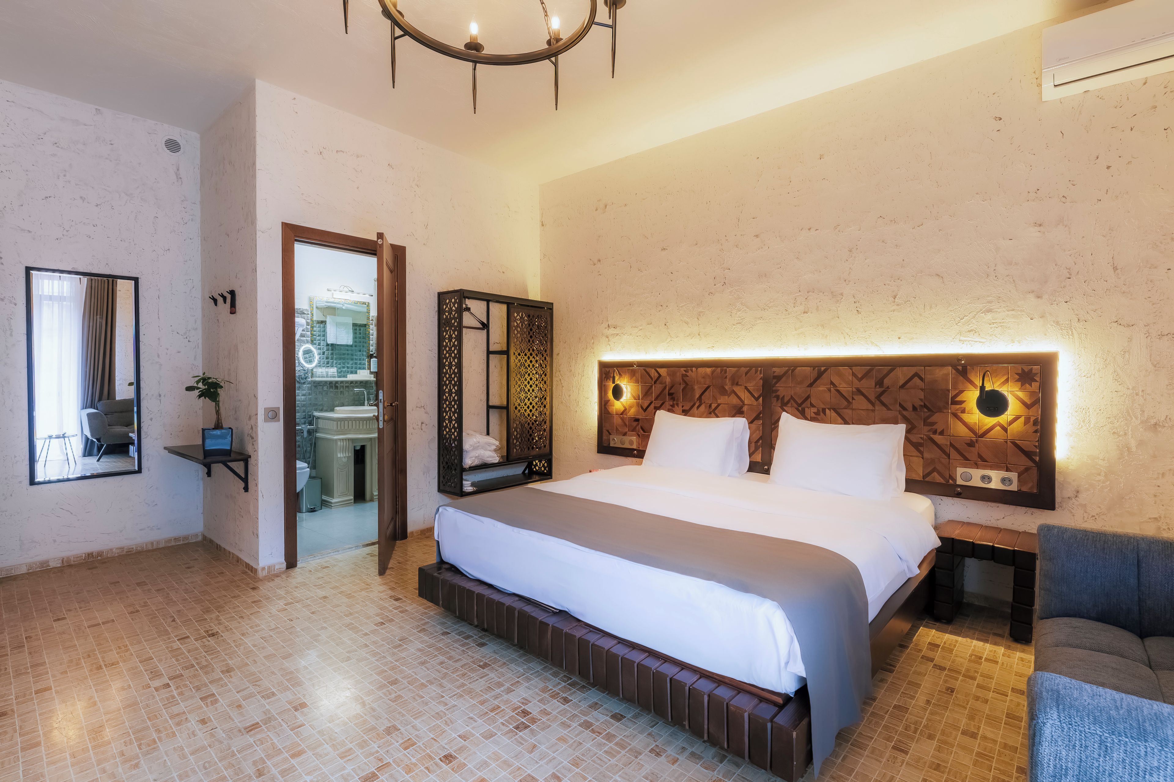 A hotel room with a large bed, a bedside table, a chair, a mirror, and a door leading to a bathroom.