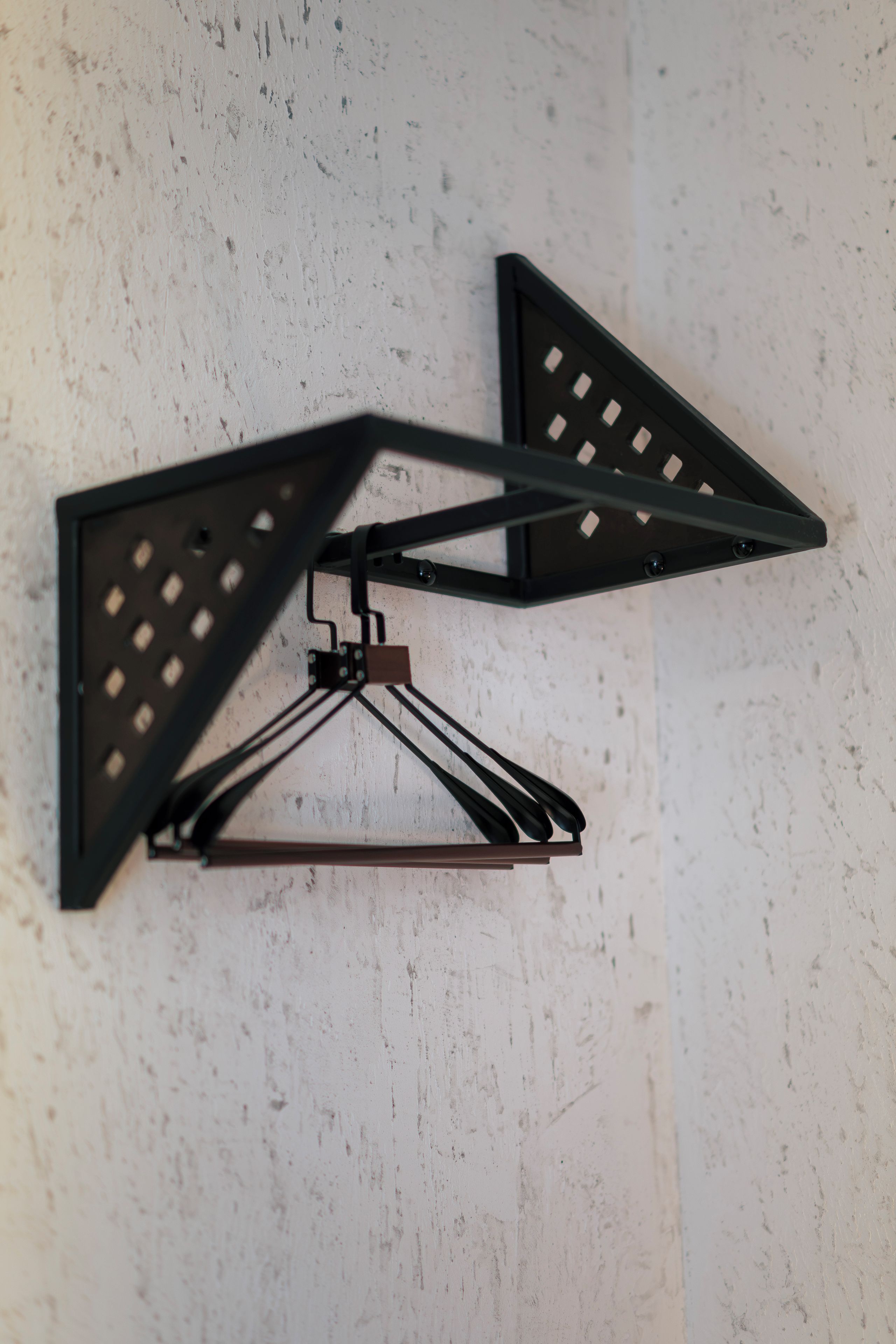 A wall-mounted light fixture with a triangular design and a central hanging rod.