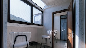A narrow corridor with a skylight, white walls, and three white chairs with black frames.