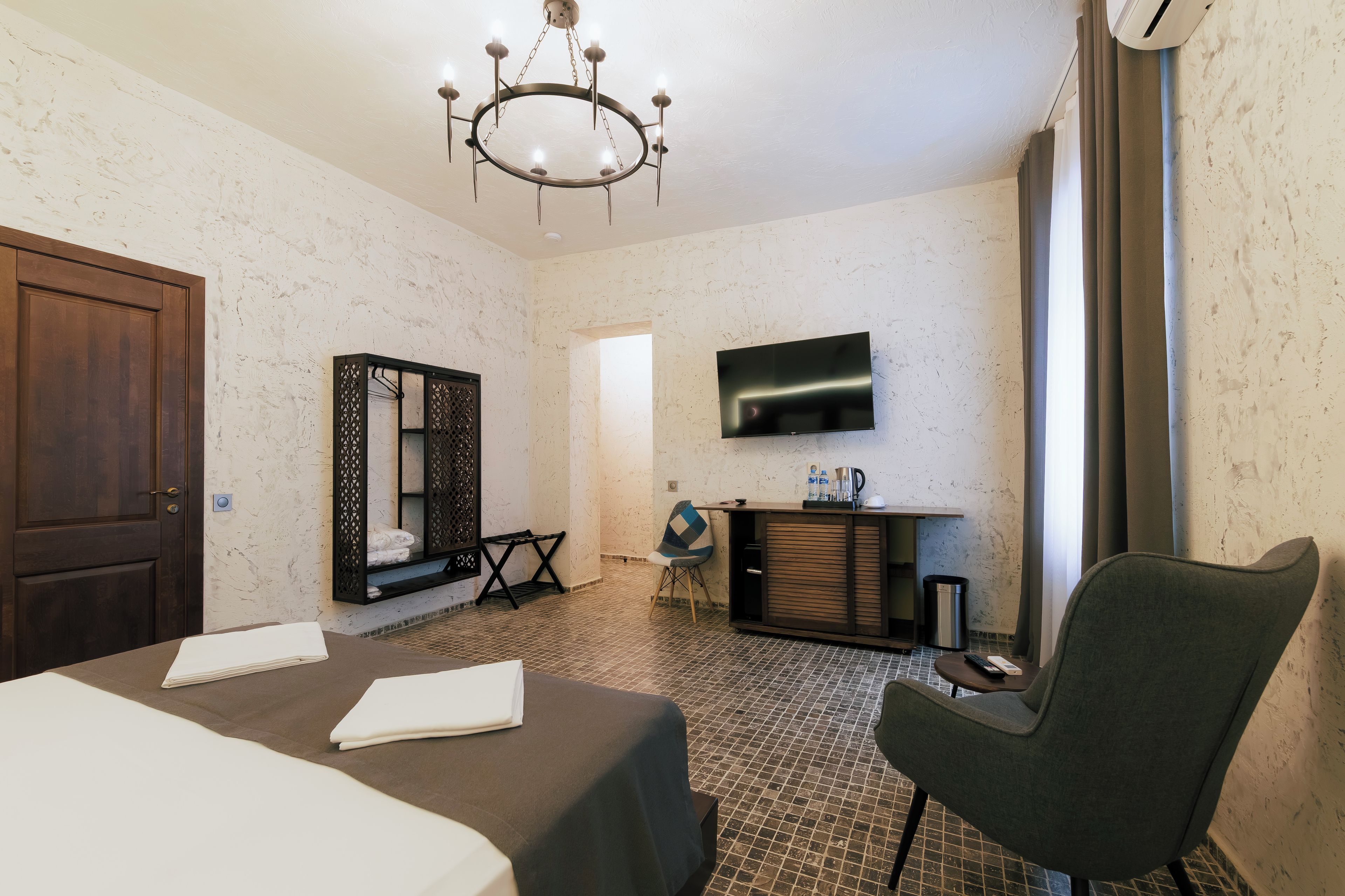 Quarto de hotel com cama, televisão na parede, armário de madeira e uma cadeira.