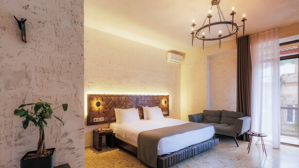 A hotel room with a large bed, a sofa, a small table, a potted plant, and a chandelier.