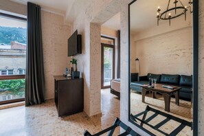 Ein modernes Hotelzimmer mit großem Fenster, einem Flachbildfernseher, einer Couch, einem Couchtisch und einem Spiegel, der den Raum widerspiegelt.