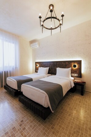 Une chambre d’hôtel avec deux lits, un lustre, un climatiseur fixé au mur et un sol carrelé.