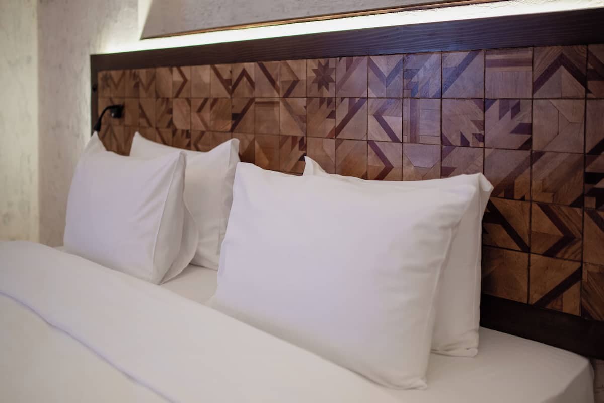 Ein Bett mit weißer Bettwäsche und Kissen, ein Kopfteil mit geometrischem Muster und eine Leuchte darüber.