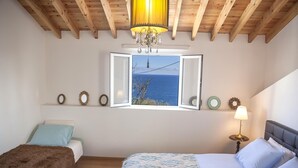 A bedroom with a large bed, a smaller bed, a window with a view of the sea, a chandelier, and wall decorations. - Water from Alto Main House (Água de Alto)