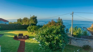 A coastal property with a well-maintained lawn, a seating area with a fire pit, and a view of the sea. - Water from Alto Main House (Água de Alto)