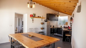 A modern kitchen with wooden beams, a dining area with a wooden table and chairs, and a small island with a sink and stools. - Water from Alto Main House (Água de Alto)