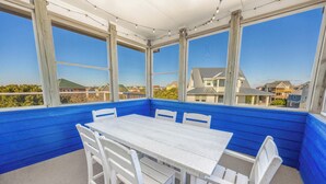 Een overdekt terras met een witte tafel en stoelen, grote ramen en uitzicht op huizen.