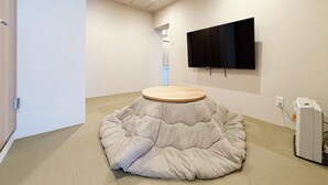 A modern room with a round wooden table, a flat-screen TV mounted on the wall, and a telephone on the floor. - Celine Kanayama 501 (Hiroshima)