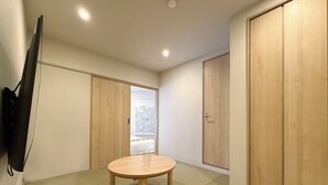 A room with a round wooden table, a TV mounted on the wall, and wooden wardrobes. - Celine Kanayama 501 (Hiroshima)