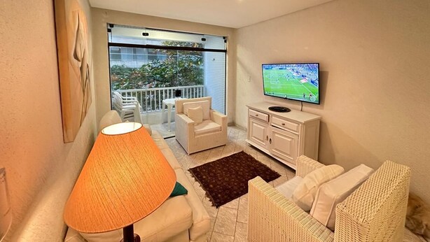 Ein gemütliches Wohnzimmer mit Sofa, Sesseln, Fernseher und einem Balkon mit Aussicht.