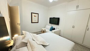 Ein Hotelzimmer mit einem Bett, einem Fernseher, einem Kleiderschrank und einem Hund, der auf dem Boden sitzt.
