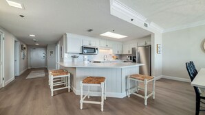 Een moderne keuken met witte kastjes, een centraal eiland met krukken, roestvrijstalen apparatuur en een houten vloer.