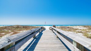 Een houten looppad dat naar een strand leidt, met heldere lucht.