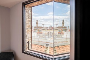 Una habitación con un amplio ventanal que ofrece vistas a un casco antiguo con torres destacadas y una plaza.