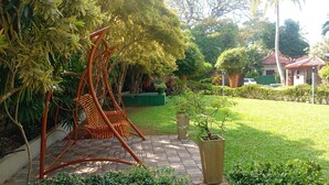 Ein Garten mit Schaukelstuhl, Topfpflanze und einem kleinen Gebäude im Hintergrund.