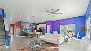 A modern living room with a white sofa, a glass coffee table, and a colorful abstract mural on the wall. - Wonderland Sleeps 14 Free Waterparks and South Facing Pool (Kissimmee)
