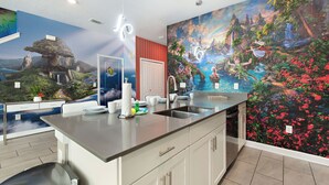 A modern kitchen with a large island, white cabinetry, and a mural depicting a tropical landscape. - Wonderland Sleeps 14 Free Waterparks and South Facing Pool (Kissimmee)