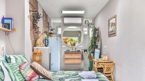 Une chambre d’hôtel de taille réduite, comprenant un lit, un petit bureau, un miroir, une armoire et une salle de bain visible à travers une porte ouverte.