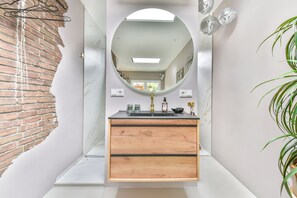 Ein Badezimmer mit einem Holzkosmetikschrank, einem runden Spiegel und einem Waschbecken.
