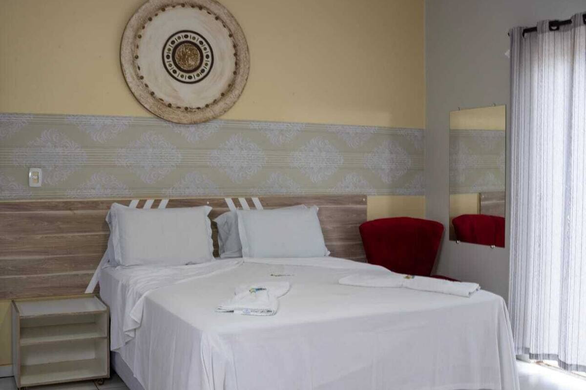A hotel room with a bed, a nightstand, a red chair, and a wall-mounted mirror.