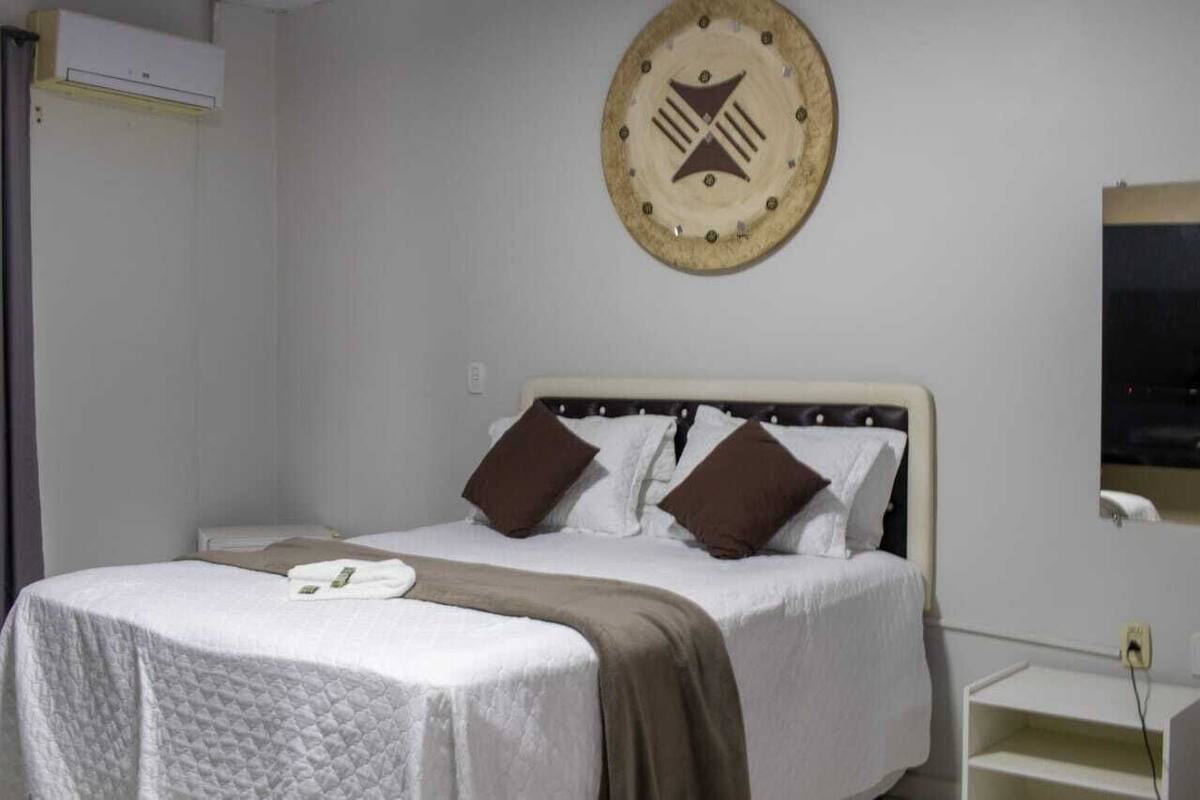 A neatly made bed with a white and brown bedspread, a brown throw blanket, and two brown pillows.