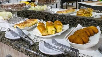 Un bufé con diferentes opciones de comida, incluyendo sándwiches, panecillos y pasteles.