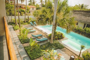 Un área de piscina con sillones de descanso y palmeras.