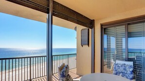 Een balkon met uitzicht op de oceaan, een tafel en een stoel met gekleurde kussens.