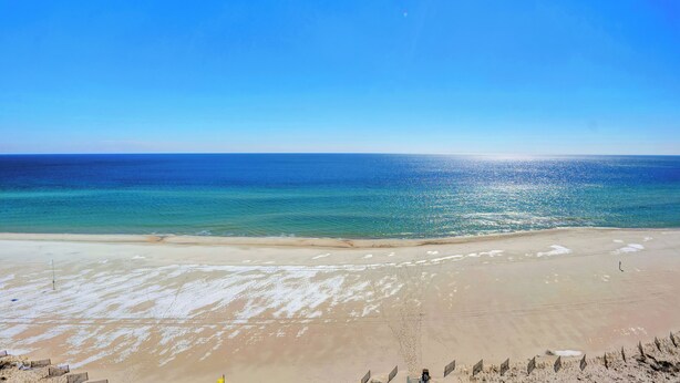 Een breed strand met helderblauw water en een zandstrand.