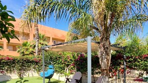 A sunny outdoor area with artificial grass, a palm tree, lounge chairs, and a blue chair. - CT 362 AL First Line Beachfront Vera Playa ID 791 (Vera)