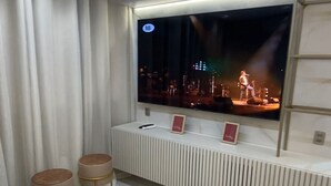 A modern living room with a flat-screen TV mounted on a wall, a sofa, and two round side tables. - Complete and Comfortable Flat (Boa Viagem Recife)
