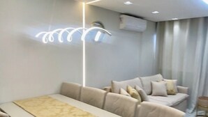 A modern dining area with a long table and chairs, a sofa, and a ceiling light fixture. - Complete and Comfortable Flat (Boa Viagem Recife)