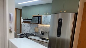 A modern kitchen with a central island, stainless steel appliances, and light green cabinetry. - Complete and Comfortable Flat (Boa Viagem Recife)