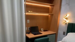A hotel room with a bed, a desk with a laptop, a green chair, and a nightstand with a lamp. - Complete and Comfortable Flat (Boa Viagem Recife)