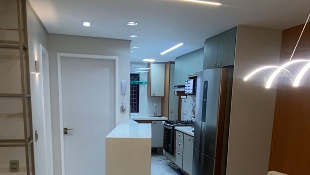 A modern kitchen with built-in appliances, a dining area with a table and chairs, and a hallway leading to a door. - Complete and Comfortable Flat (Boa Viagem Recife)