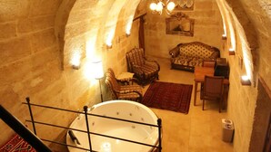 Un intérieur en pierre avec des arches, comprenant une baignoire, un coin salon et des tapis à motifs.