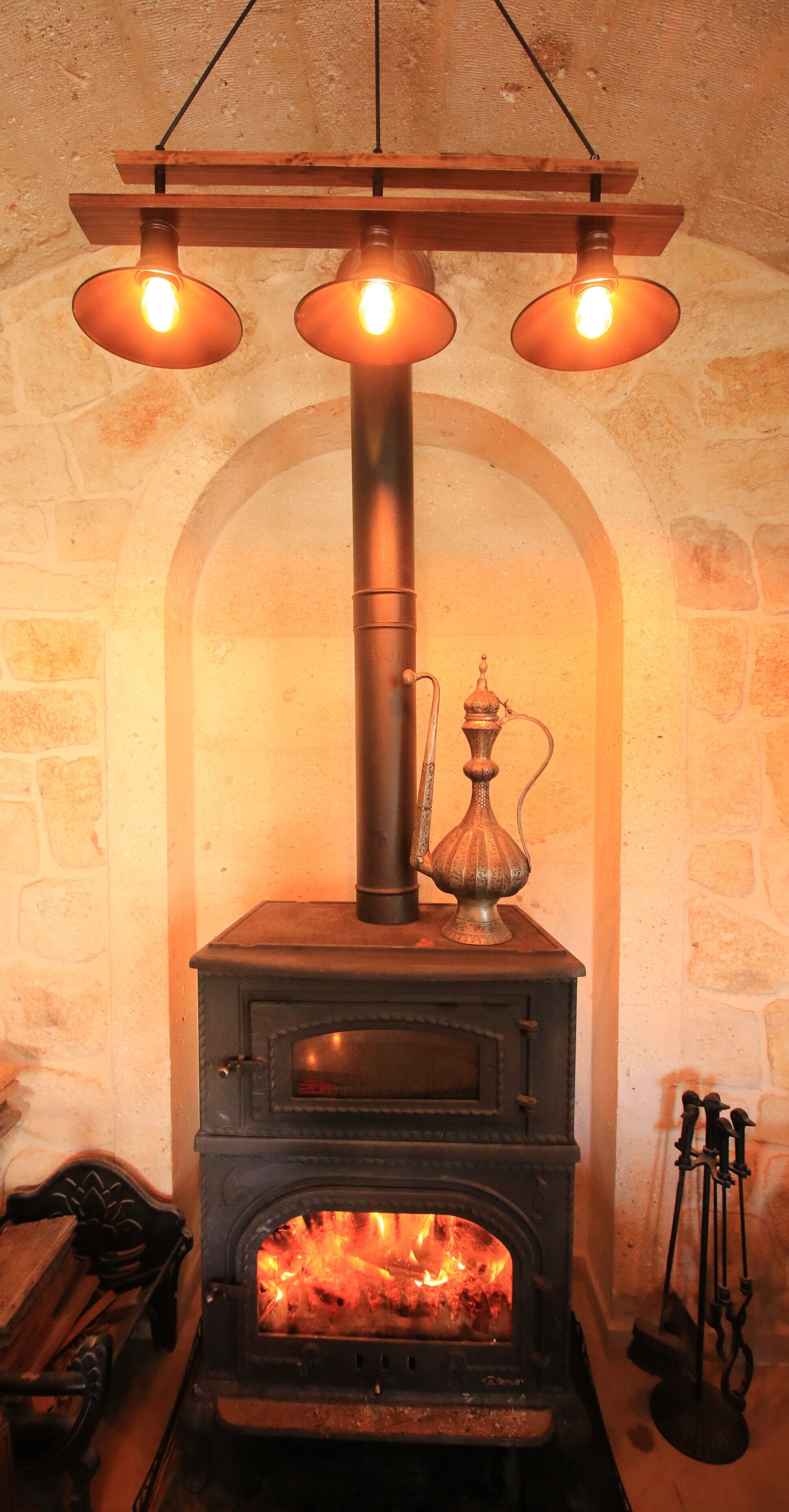 A wood-burning stove with three hanging lights above it.
