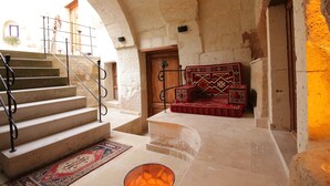 Un escalier en pierre mène à une pièce où se trouve un foyer, un tapis à motifs et un canapé rouge et noir à motifs.