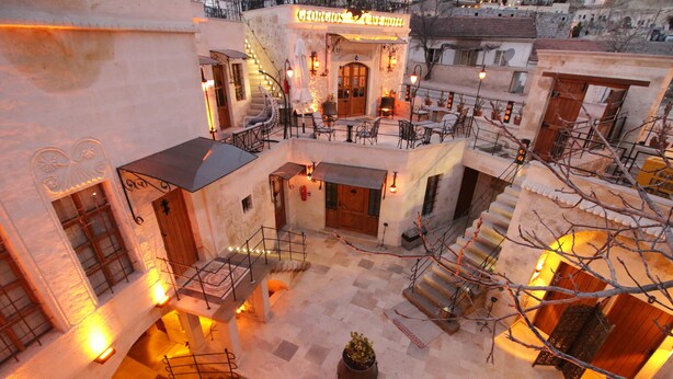 Une cour intérieure à plusieurs niveaux, dotée d’un espace extérieur aménagé avec des sièges, d’un escalier central et d’une enseigne indiquant « Hôtel Giorgos ».