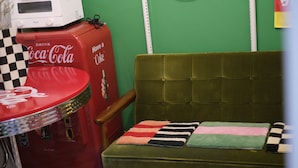 Un sofá verde antiguo con una mesita de cuadros al lado, una máquina expendedora roja de Coca-Cola y un microondas encima.